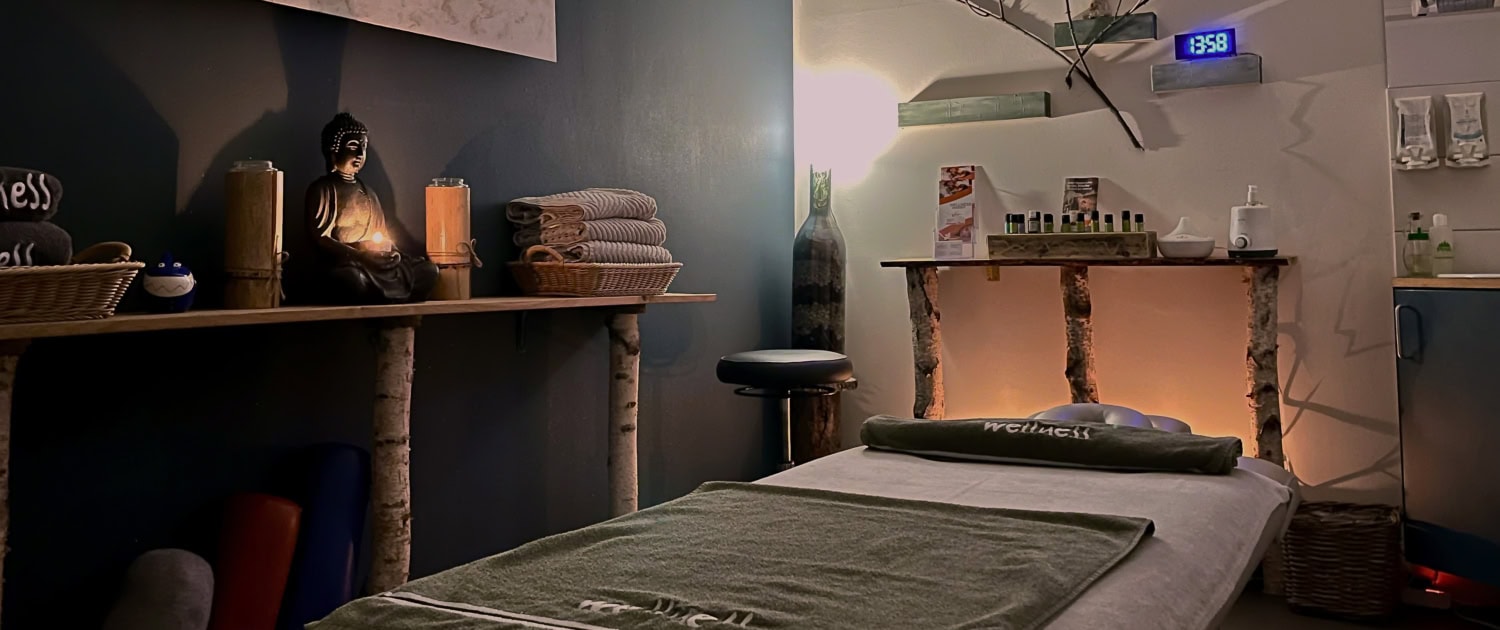 Stimmungsvoll eingerichteter Wellnessraum mit Massageliege, Handtüchern und Dekoration.