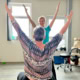 Physiotherapeutin macht gemeinsam mit einer Patientin eine Übung mit erhobenen Armen im Therapieraum.