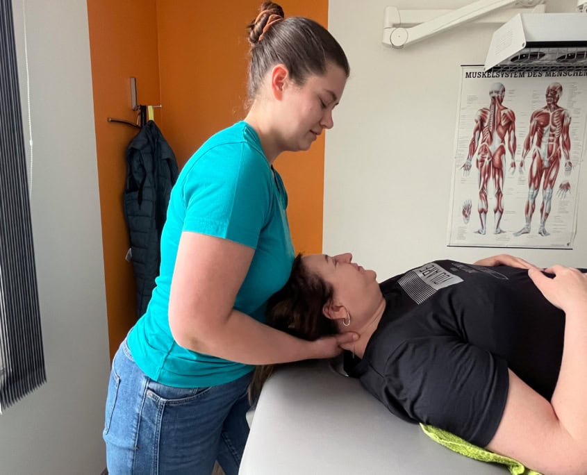 Physiotherapeutin behandelt den Nacken einer liegenden Patientin in einem Behandlungsraum.